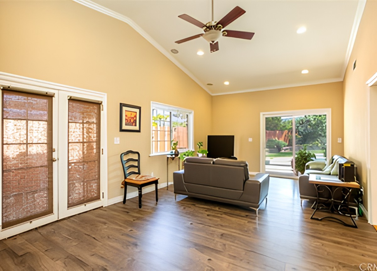 A spacious and well-lit living room with a cozy sofa, large windows, and a ceiling fan.