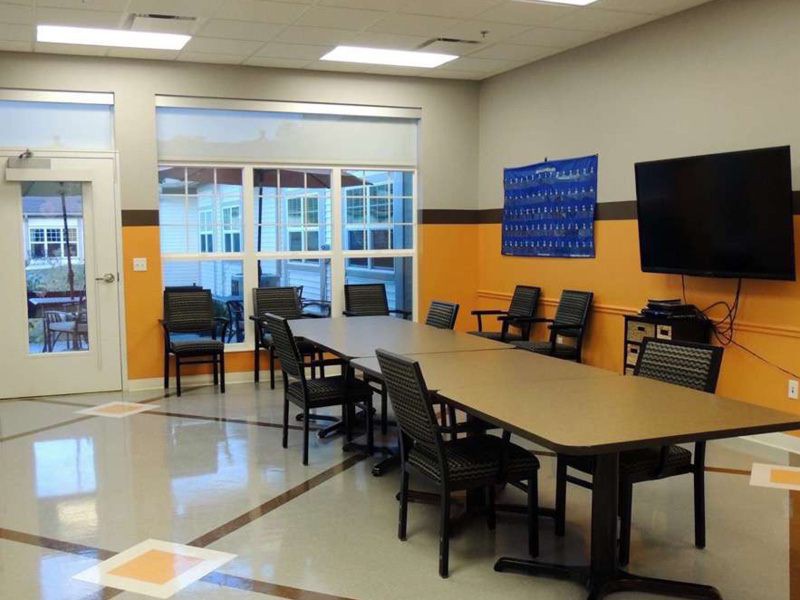 A modern conference room with a large meeting table and chairs, featuring a television and a spacious window.