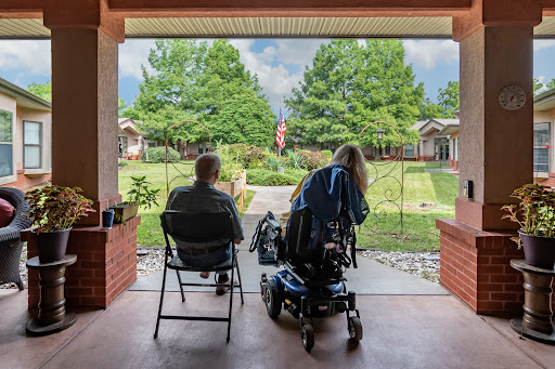 Two individuals enjoying a peaceful moment on the porch, overlooking a green landscape with an American flag in view.