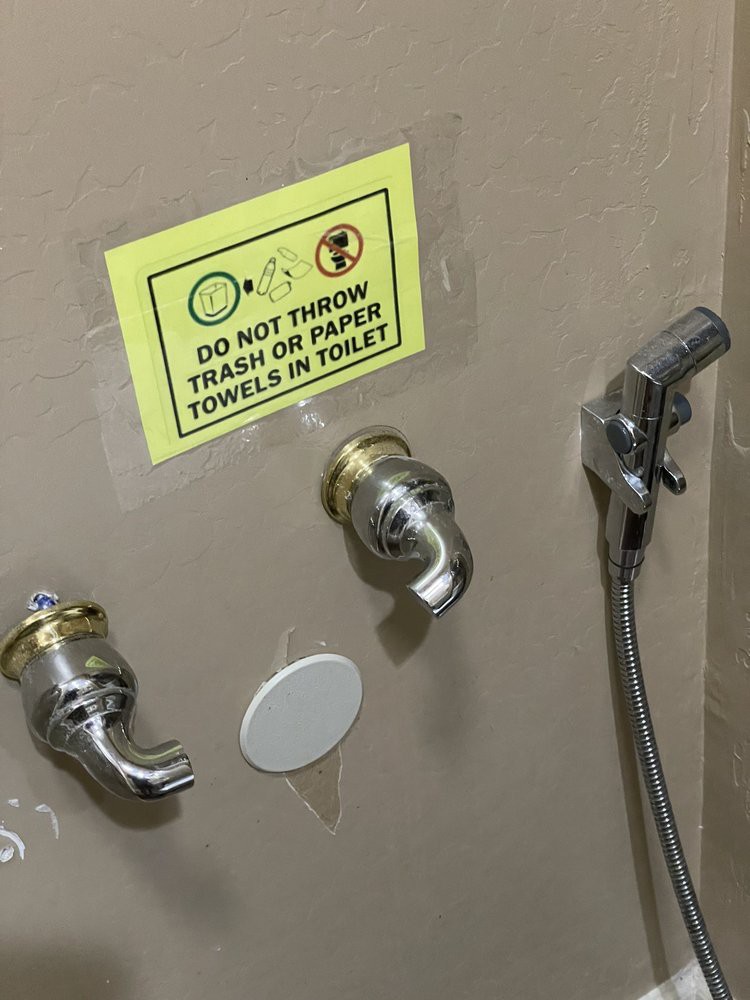 Wall-mounted faucets and a bidet spray with a warning sign in a bathroom.