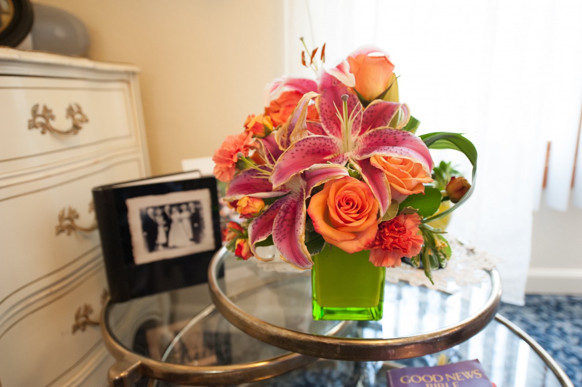A vibrant bouquet of pink lilies and orange roses in a green vase on a glass table.