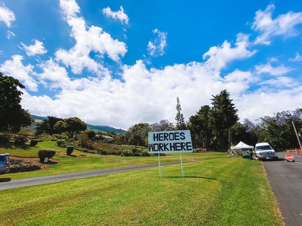 A scenic outdoor landscape featuring a sign on a grassy field under a blue sky with clouds.