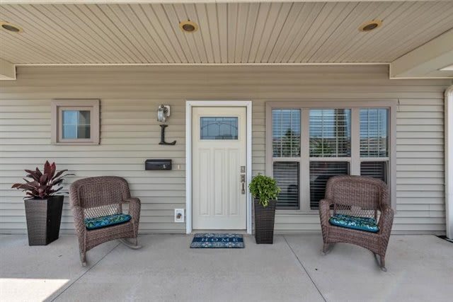 A cozy front porch with two chairs, a white door, and a decorative plant.