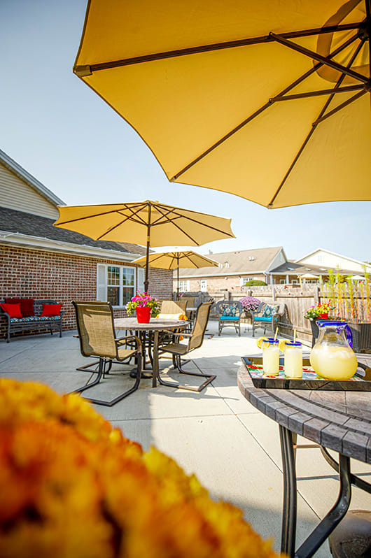 A sunny patio with tables and chairs under yellow umbrellas, decorated with vibrant flowers.