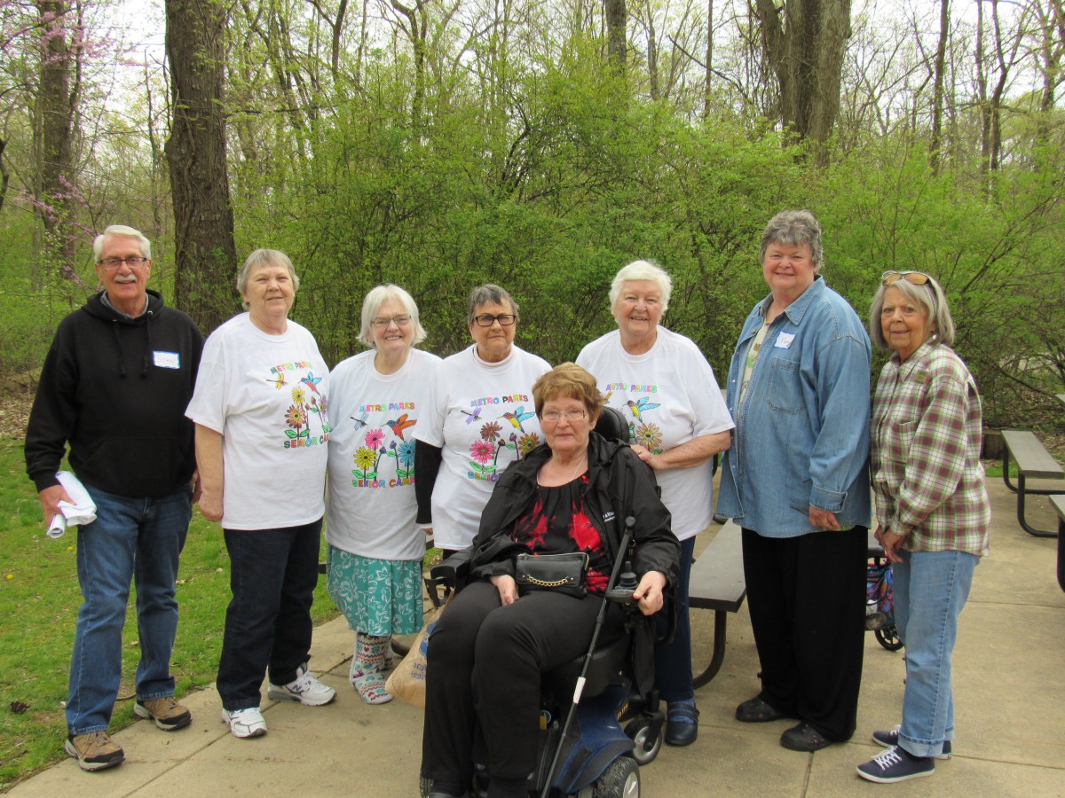 A group of adults posing for a photo outdoors in a park, with one individual seated in a wheelchair.