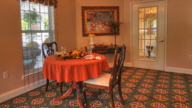 A cozy dining room with an orange tablecloth, elegant chairs, and decorative elements.