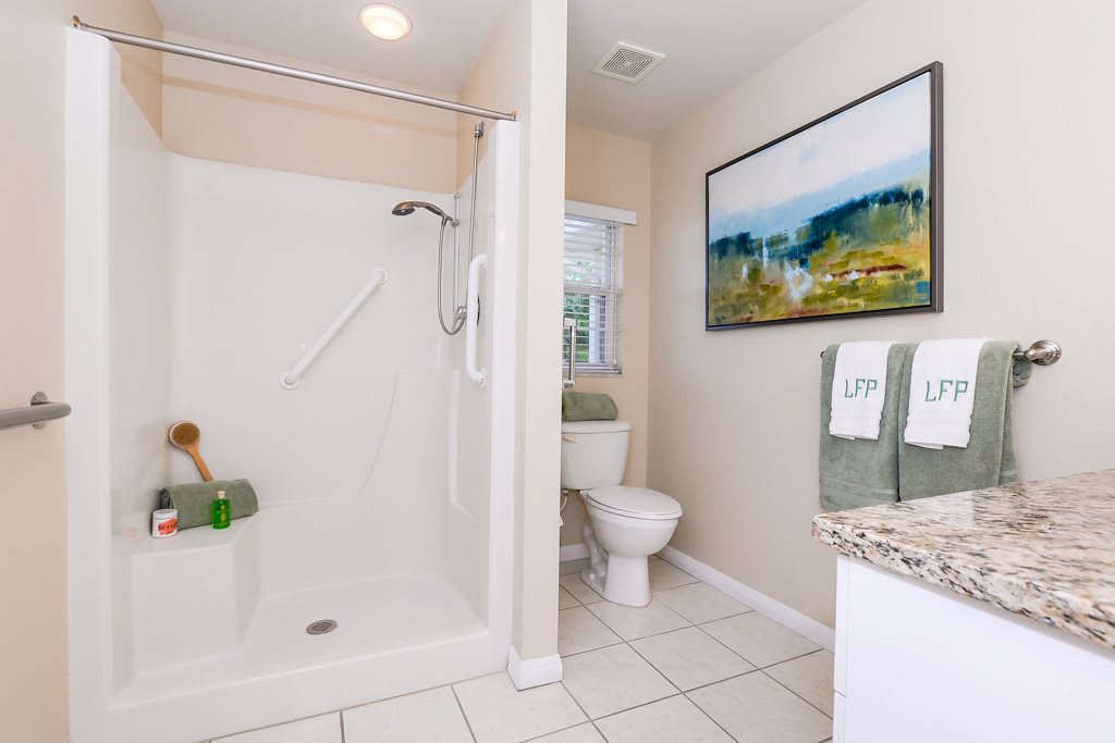 A clean bathroom with a shower, toilet, and sink, featuring decorative towels and artwork.