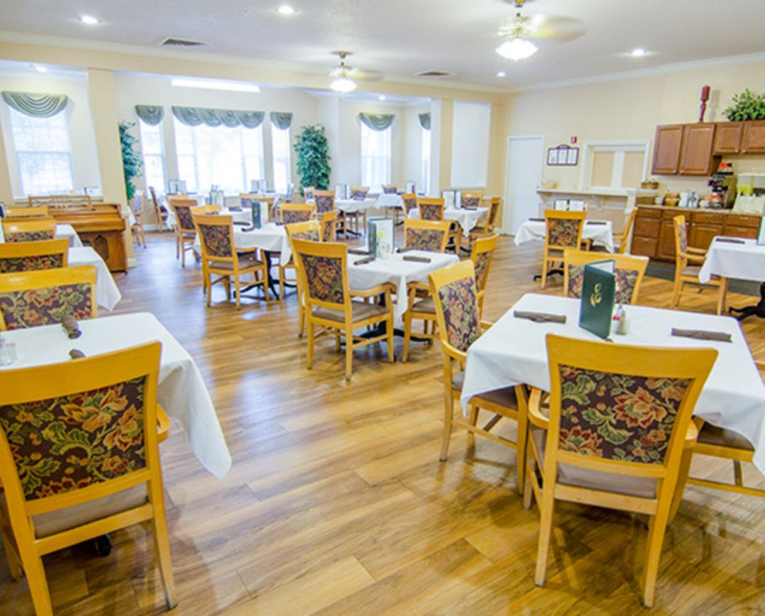 A bright and spacious dining room with neatly arranged tables and chairs, featuring wood flooring.
