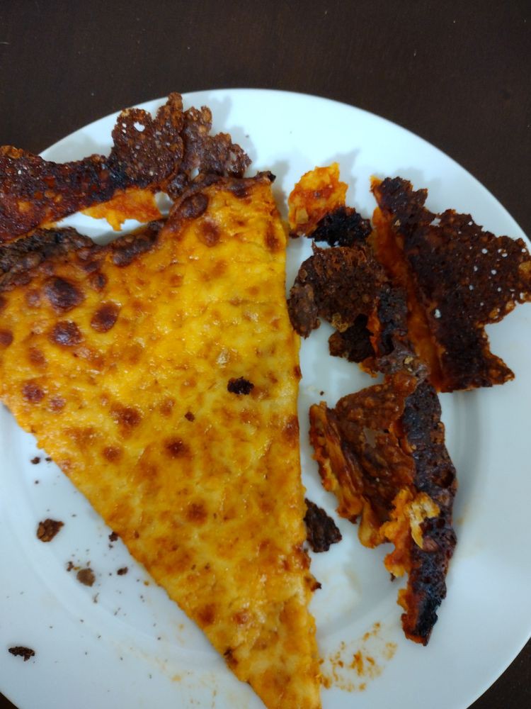 A slice of pizza with crispy, baked cheese edges on a white plate.