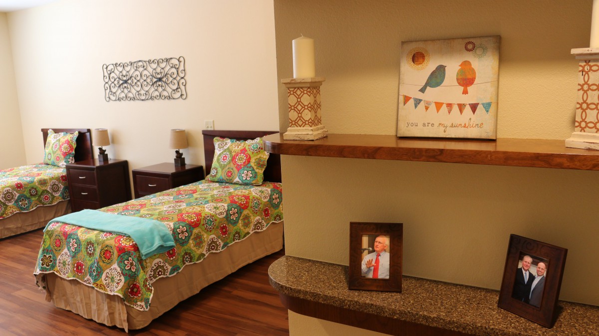 A cozy bedroom with colorful bedding, featuring a decorative shelf with artwork, a candle, and a framed photo.