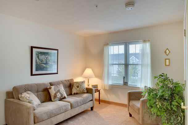 A cozy living room with a sofa, armchair, and lamp by the window.