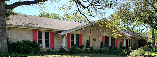 A charming single-story house with red shutters and butterfly decor, surrounded by lush greenery.