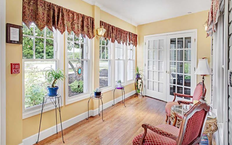 A bright sunroom with large windows, French doors, and potted plants on stands.