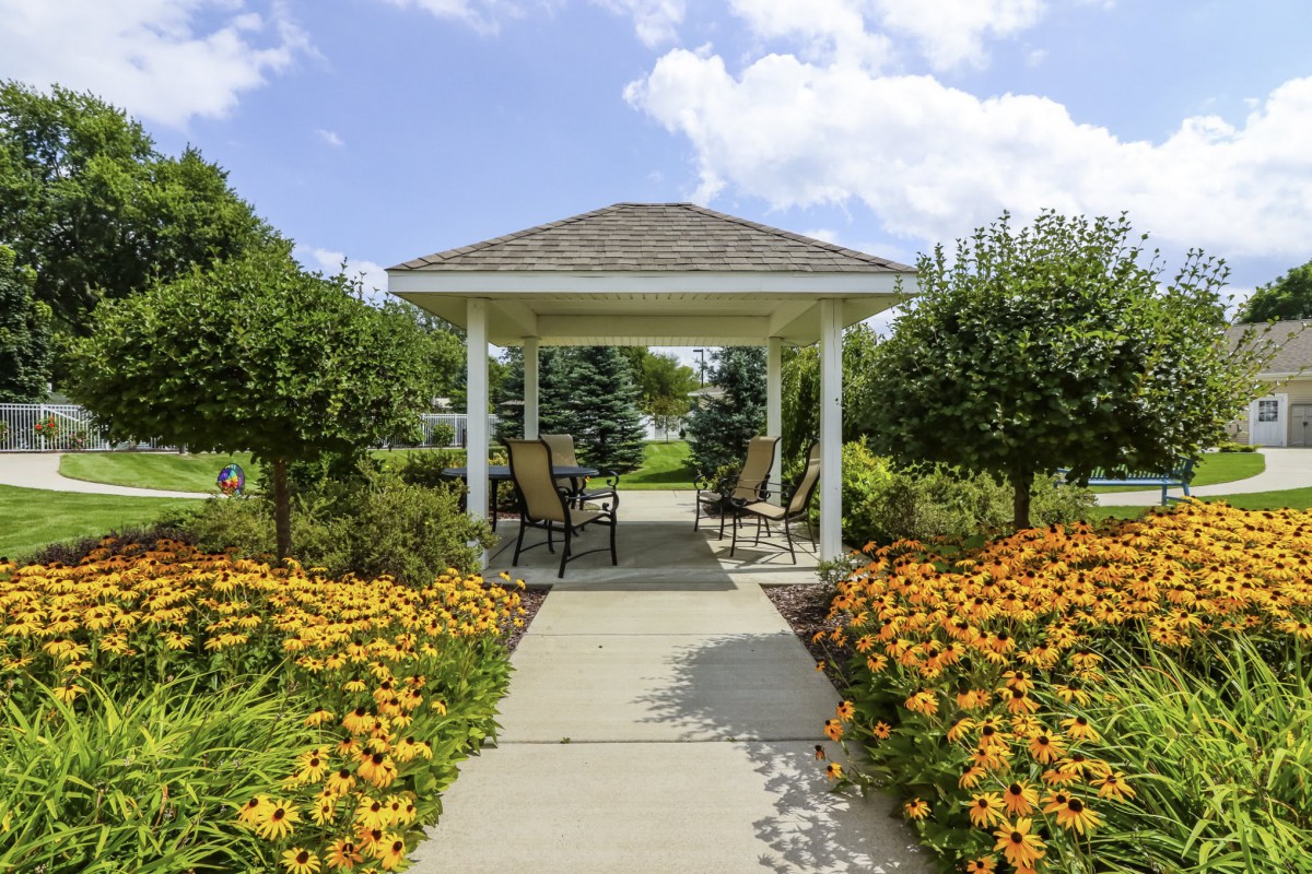 A charming garden gazebo surrounded by vibrant flowers and greenery on a sunny day.