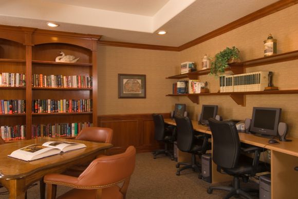 A cozy office space with bookshelves and computers, featuring wood furniture and comfortable chairs.