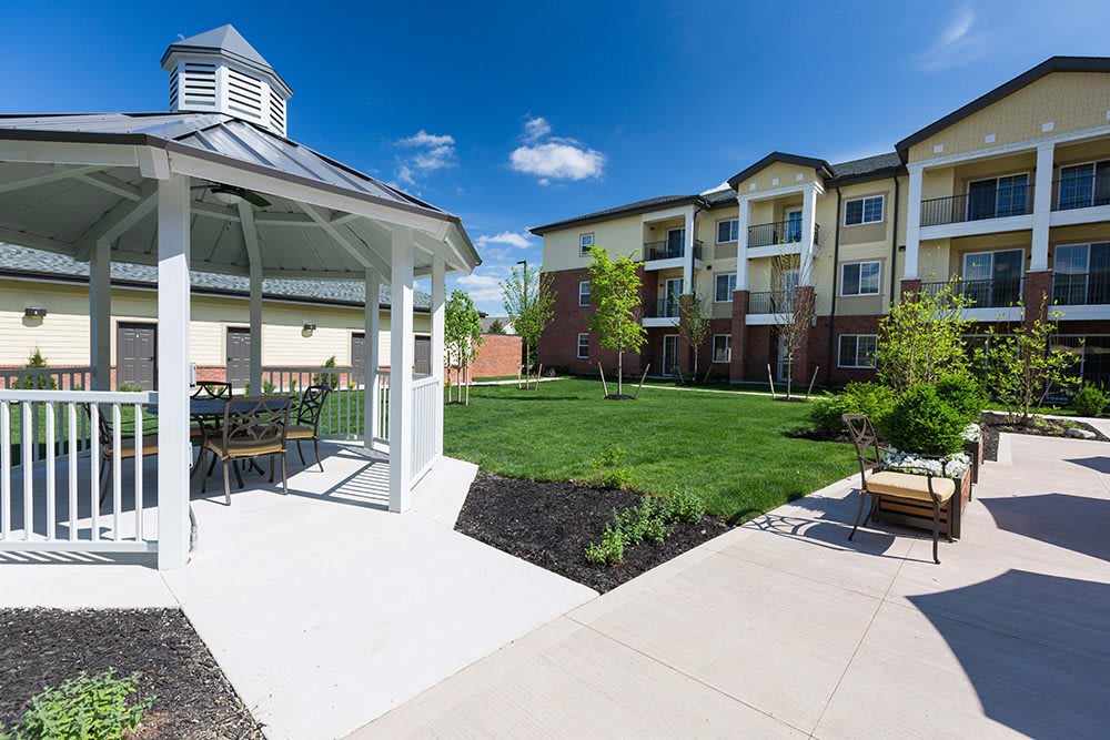 A well-maintained apartment complex featuring a gazebo, green lawn, and outdoor seating under a clear blue sky.