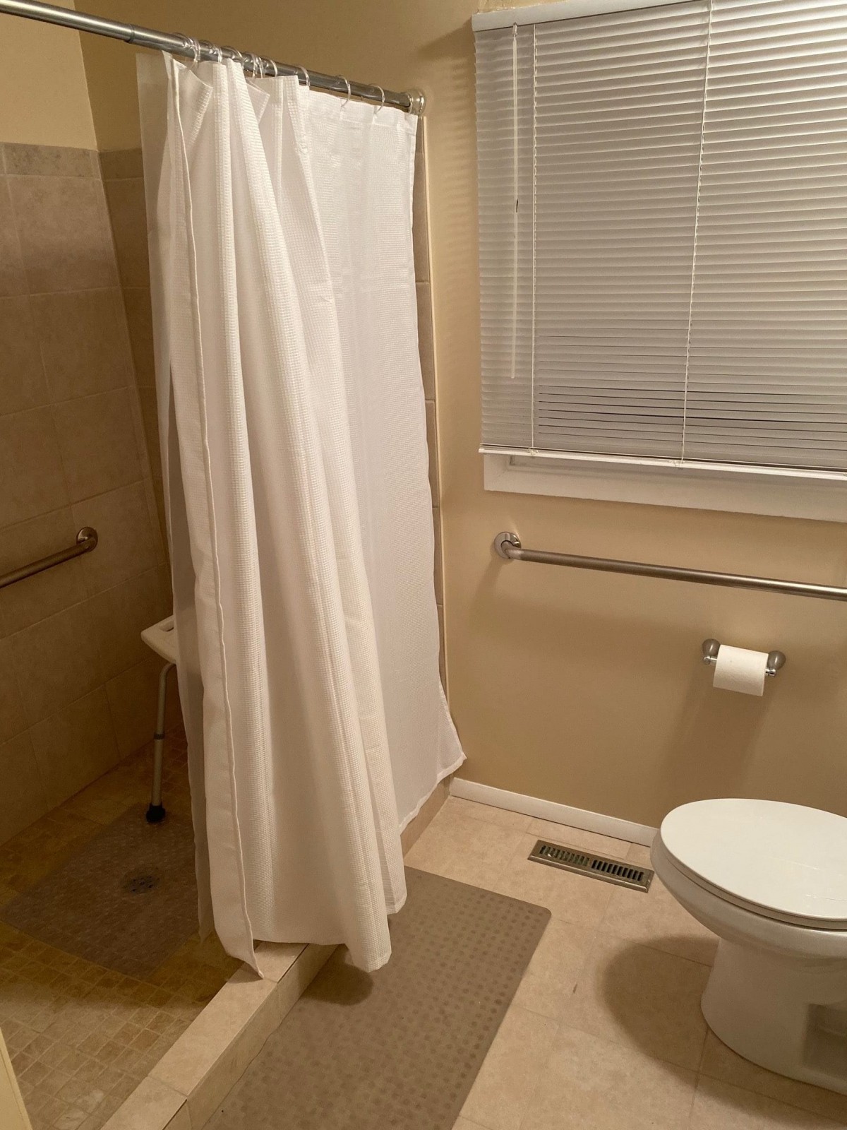 A clean bathroom with a shower, toilet, and window blind.