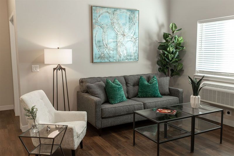 A modern living room featuring a grey sofa with green pillows, a white armchair, stylish coffee table, large floor lamp, and decorative wall art.