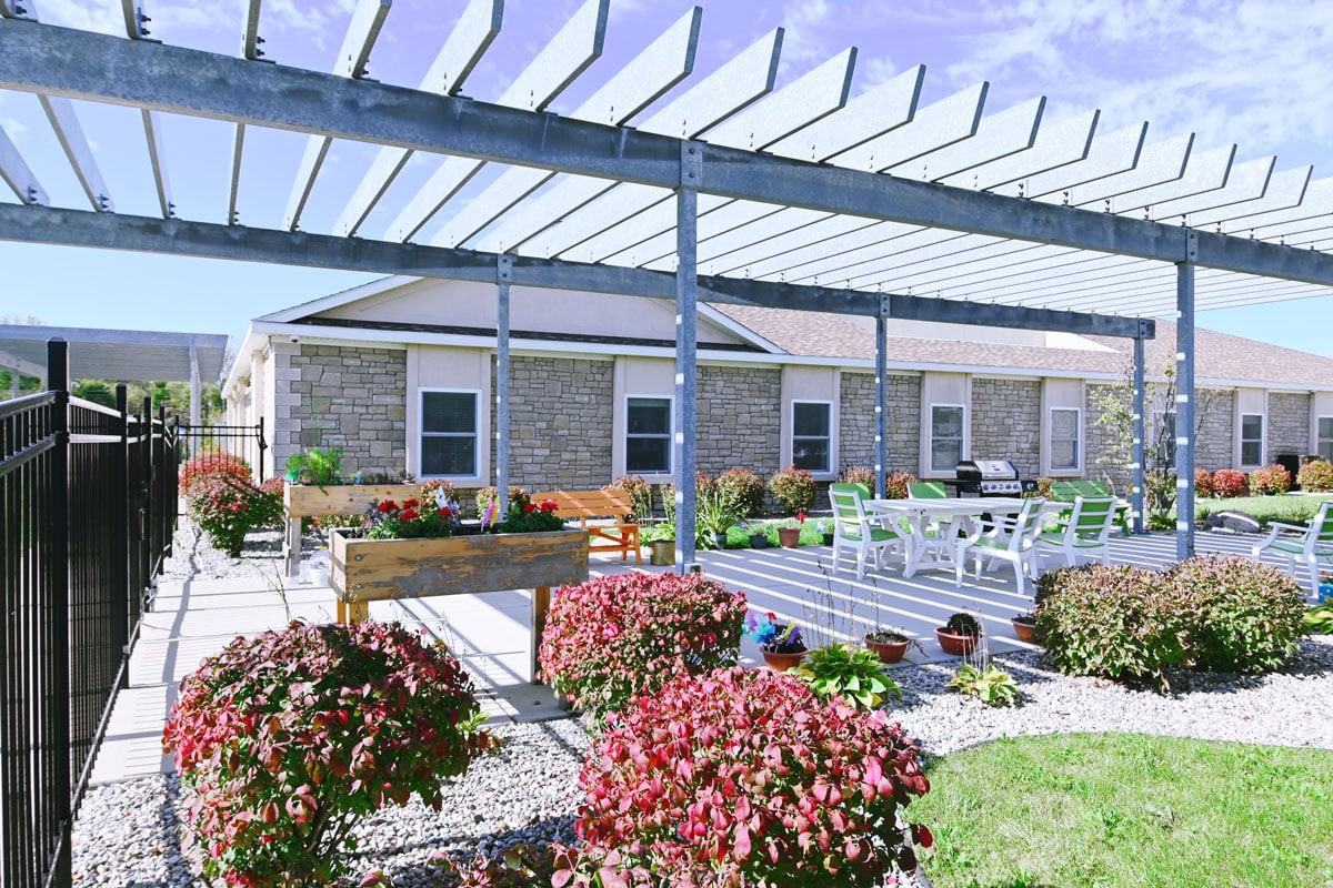 A peaceful patio with a pergola, surrounded by vibrant flowers and outdoor seating.
