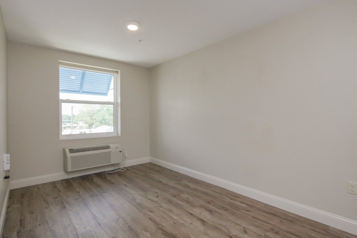 An unfurnished room with a large window, wood flooring, and an air conditioning unit.