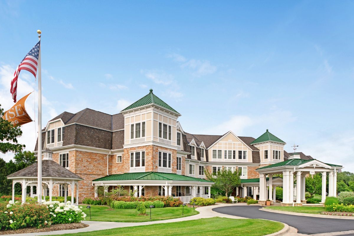 A large, elegant residential building with a neatly landscaped lawn and clear blue sky.