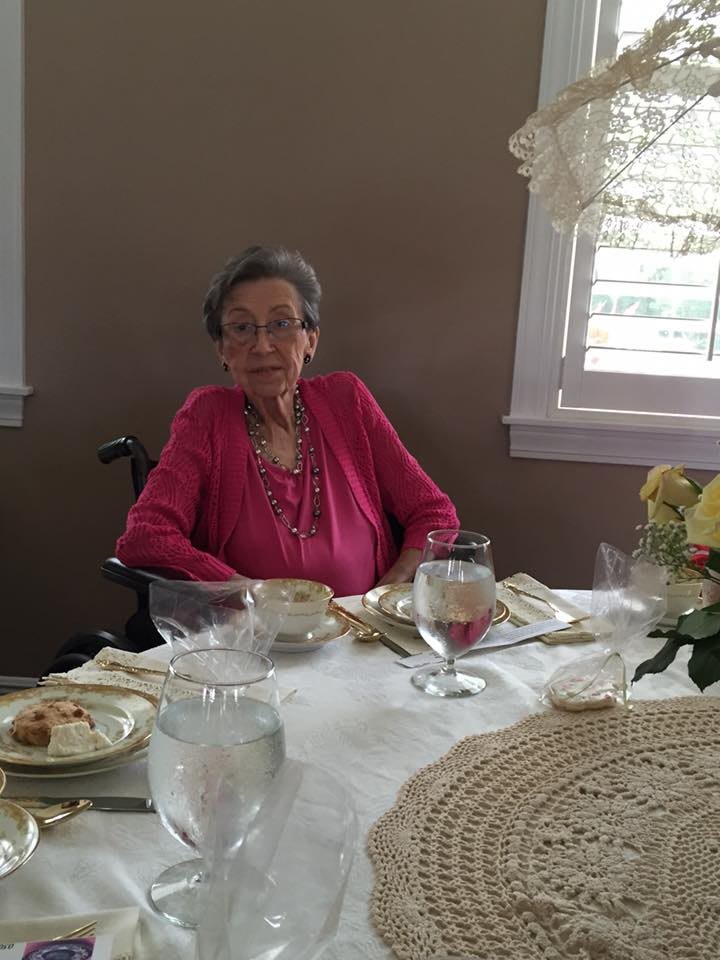 An elderly woman sitting at a dining table with a tea set in a cozy room.