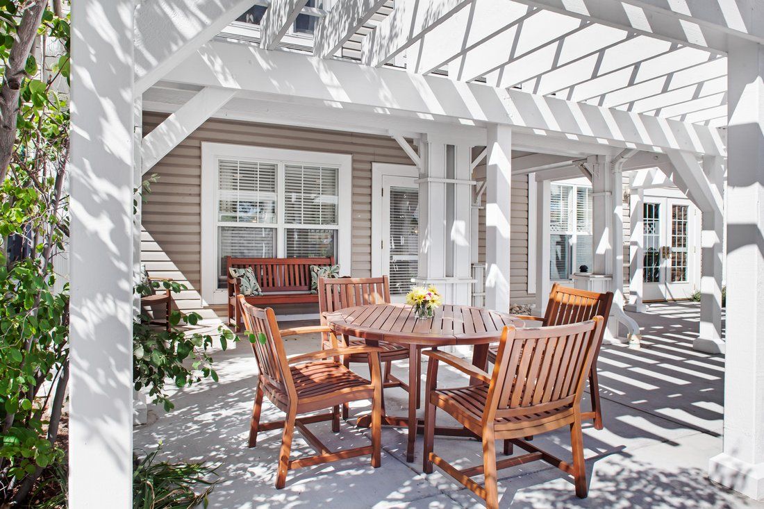 A sunlit patio with wooden furniture under a white pergola.