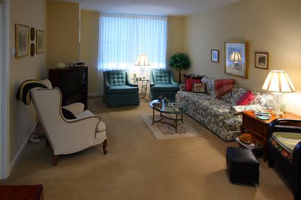 A cozy living room with a floral sofa, two armchairs, a coffee table, and soft lighting.