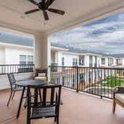 A balcony with a table and chairs overlooks an apartment complex under a cloudy sky.
