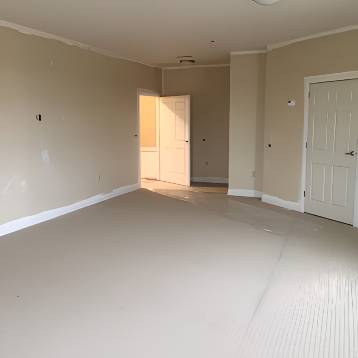 An empty room with neutral-colored walls and a carpeted floor, featuring a closed door and natural light coming through an open doorway.