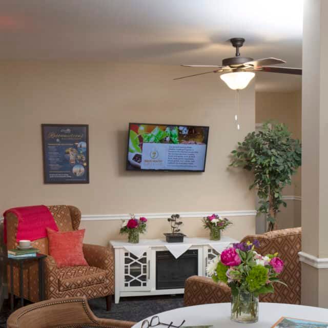 A cozy living room with comfortable seating, a television mounted on the wall, and vibrant floral decor.