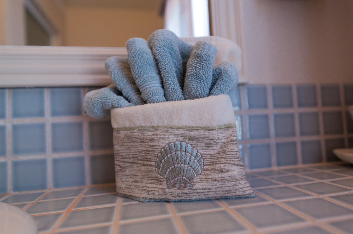 A neatly arranged set of blue towels in a holder with a shell motif, placed on a tiled bathroom surface.
