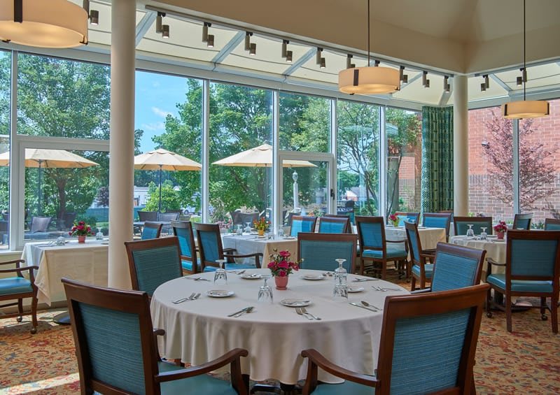 A well-lit restaurant dining area with elegantly set tables and a view of the outdoor patio.