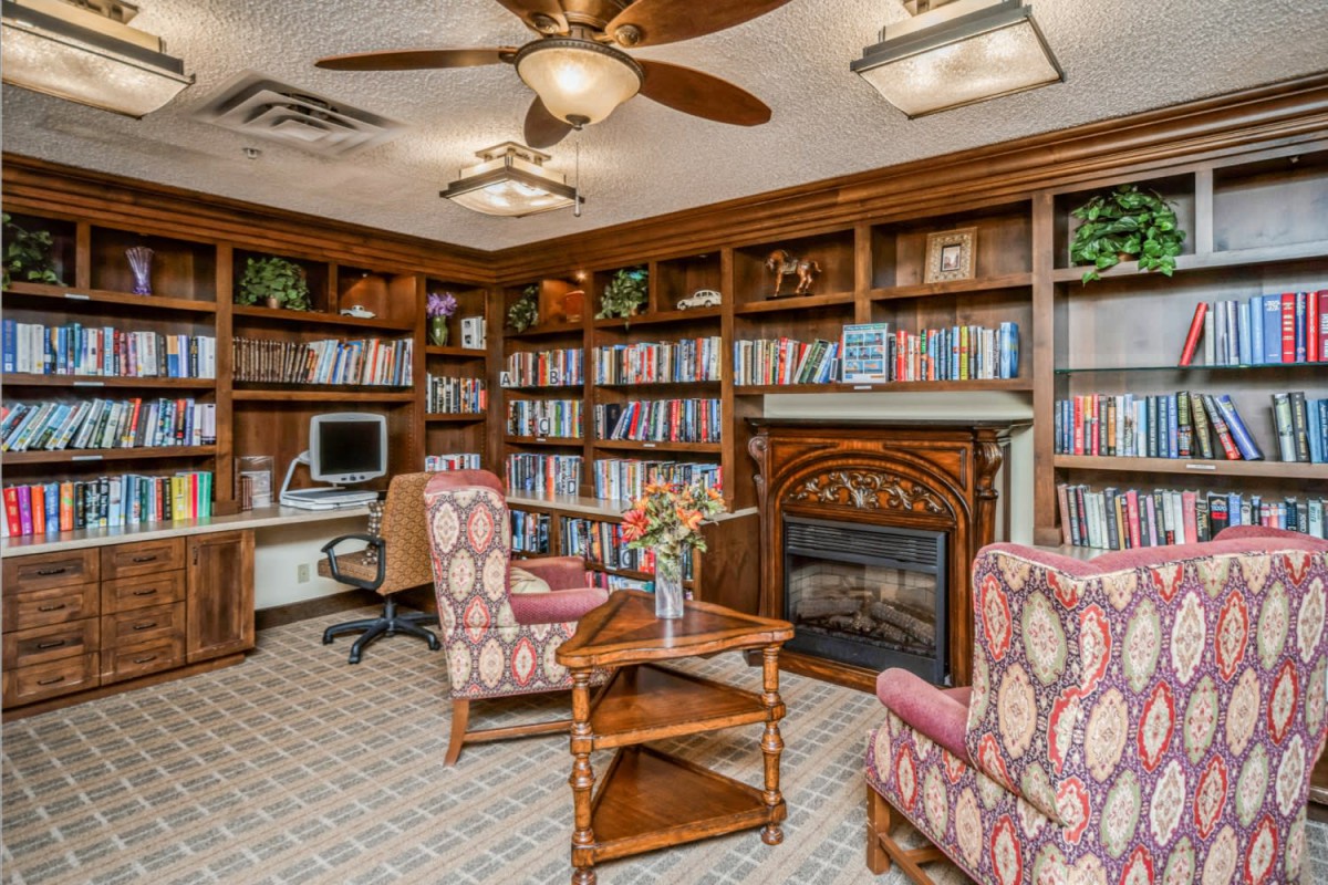 A cozy library room with bookshelves, a fireplace, and comfortable seating.