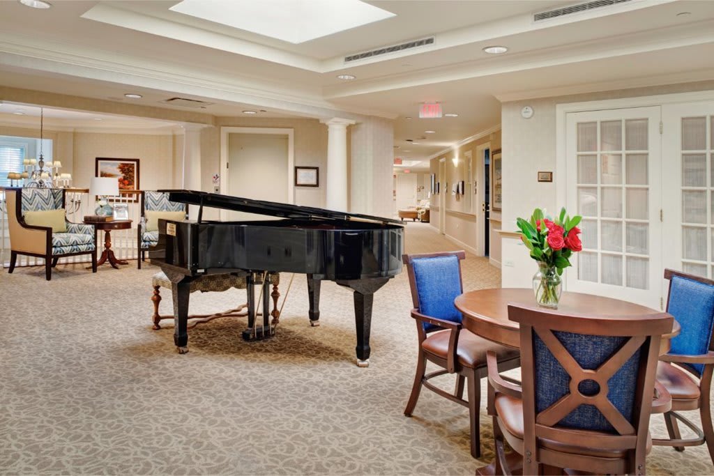 A well-lit lobby area featuring a grand piano, wooden table and chairs, and a vase of flowers on the table.