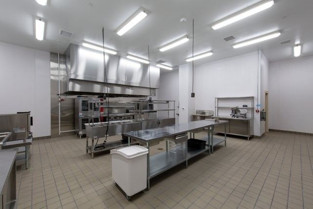 An empty industrial kitchen with stainless steel workstations and appliances.