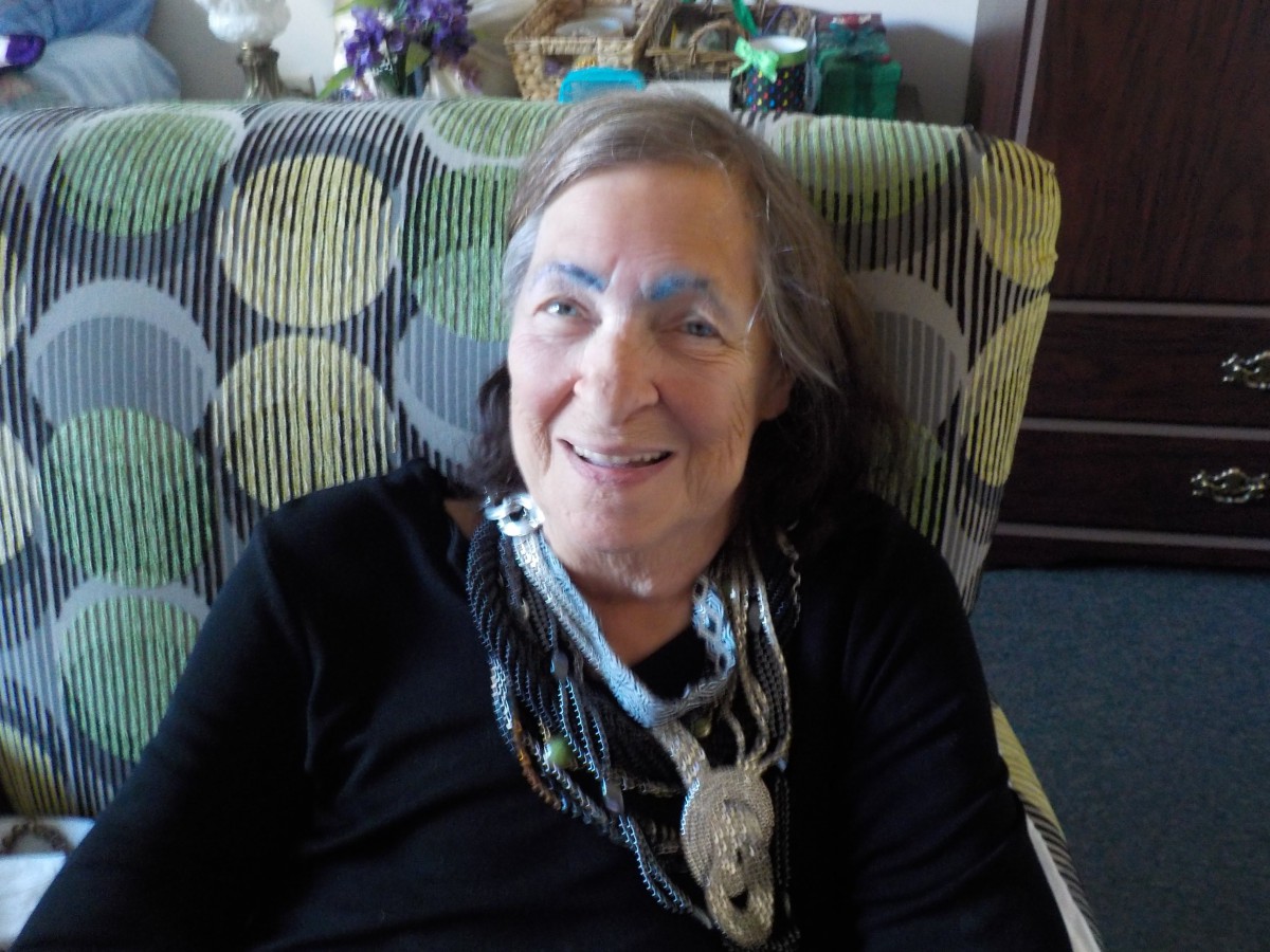 A woman sitting indoors, smiling and wearing a necklace.