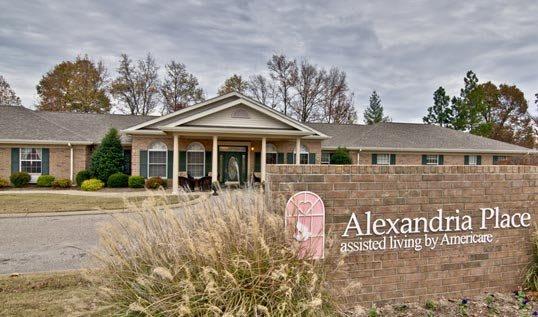 A brick building with an entrance and a sign in front, surrounded by landscaping under an overcast sky.
