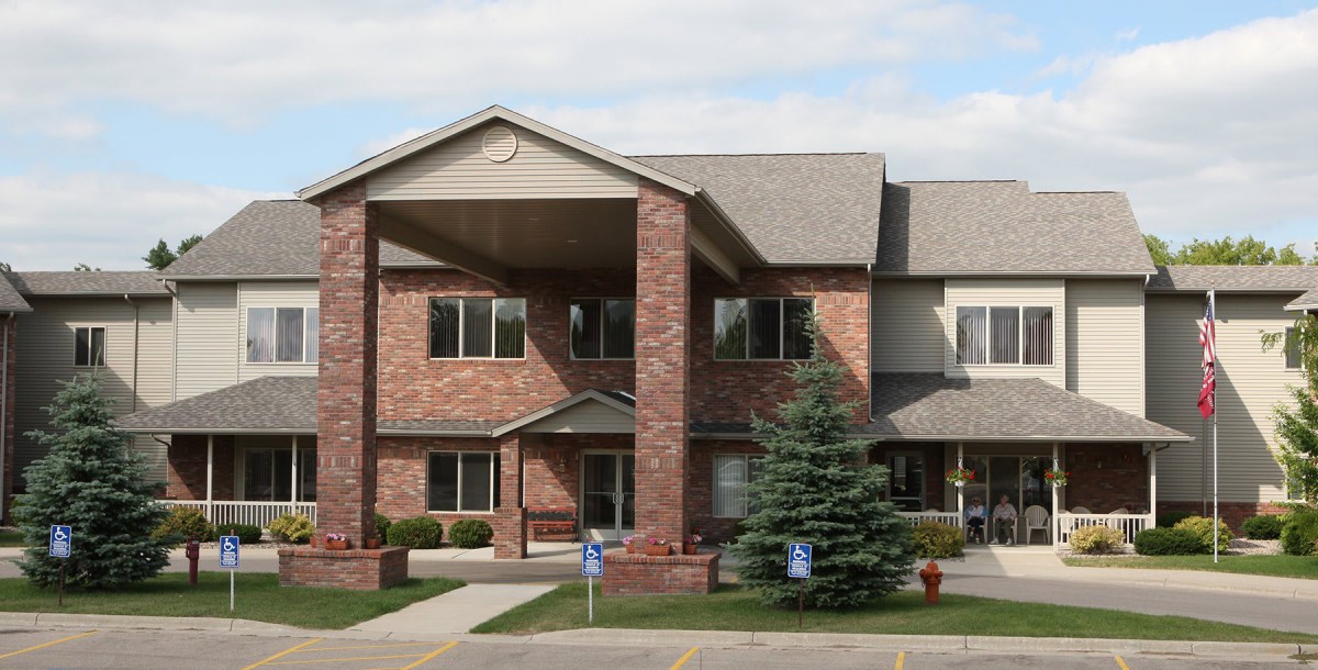 A two-story brick residential building with a pitched roof and a tree in front.