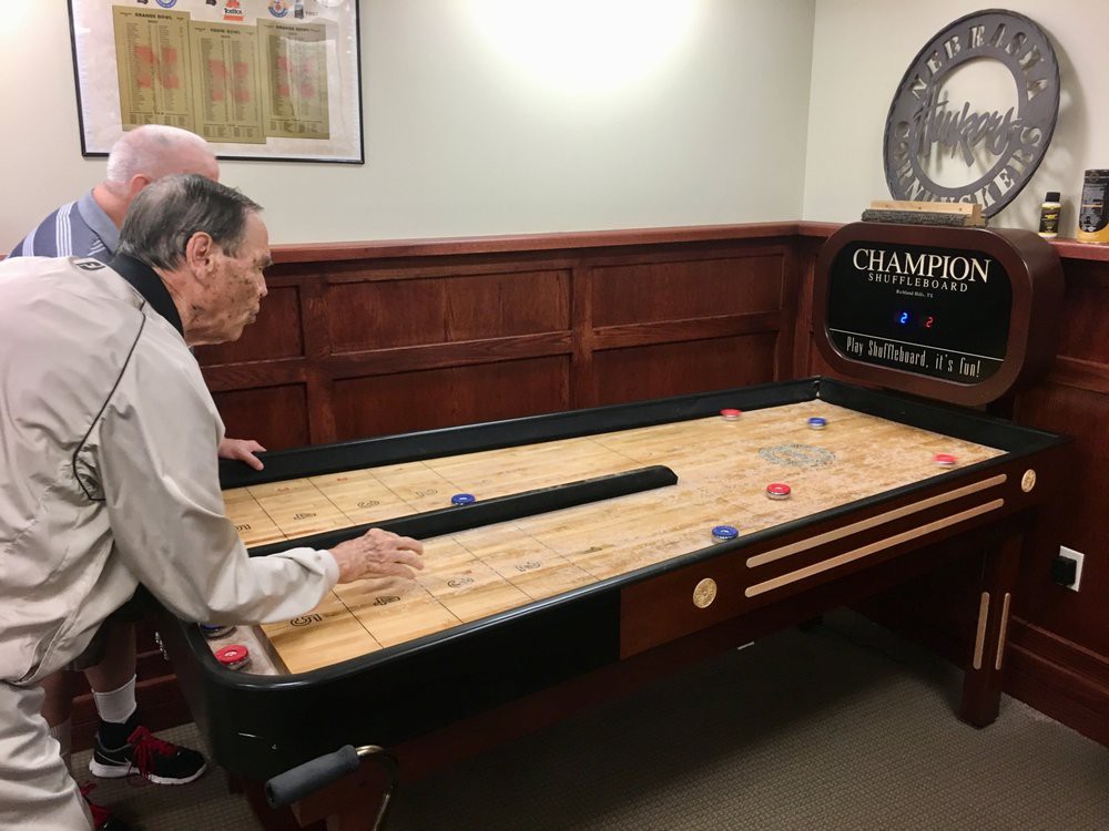 Two people playing a game of shuffleboard indoors.