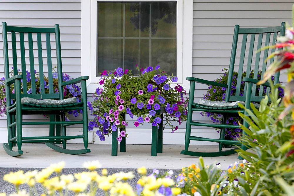 A cozy front porch with green rocking chairs and vibrant purple flowers in bloom.