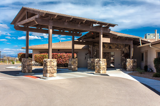 A modern entrance of a building featuring a wooden pergola and stone pillars, surrounded by well-maintained landscaping.