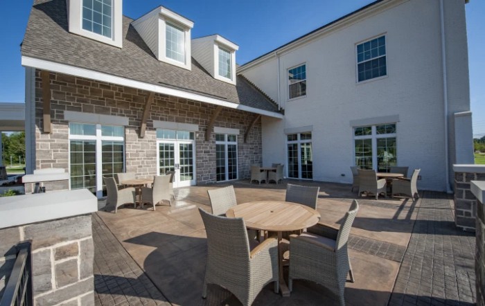A sunny patio area with tables and chairs in front of a building.