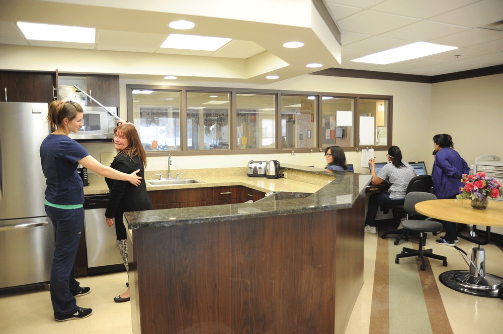 A busy office reception area with people working at desks and engaging in conversation.
