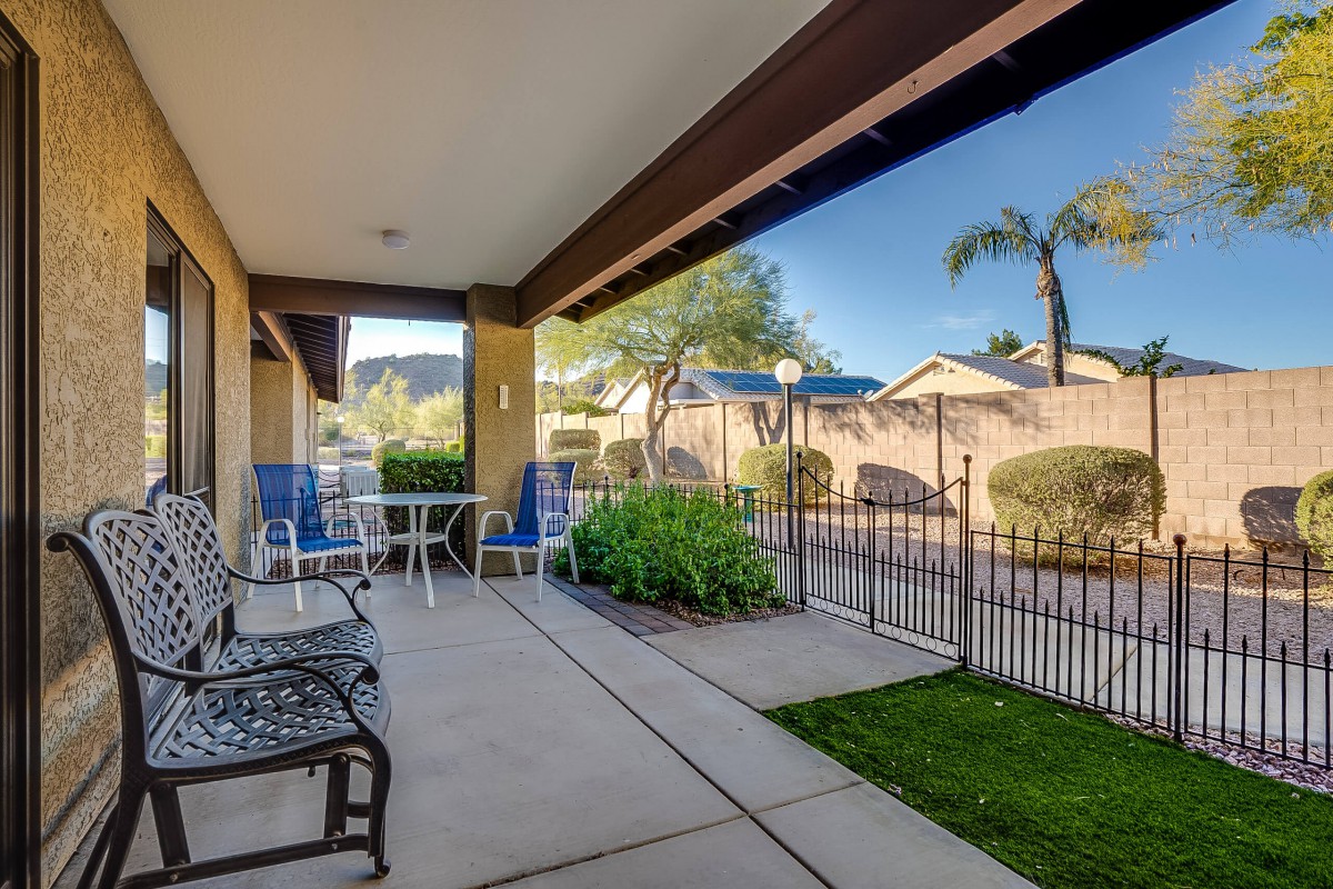 A sunny residential patio with chairs and a table, overlooking a garden and fenced yard.