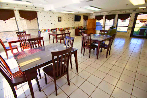 A spacious and empty dining area with wooden tables and chairs, featuring tiled flooring and natural light coming in.
