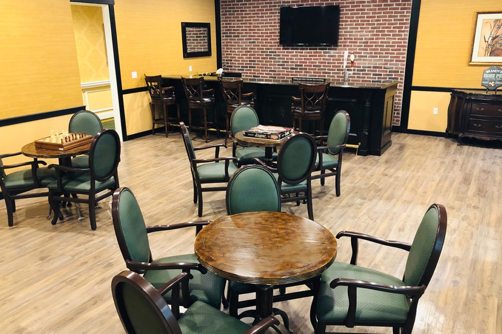Cozy indoor lounge with tables and chairs, featuring a bar and television on a brick-accented wall.