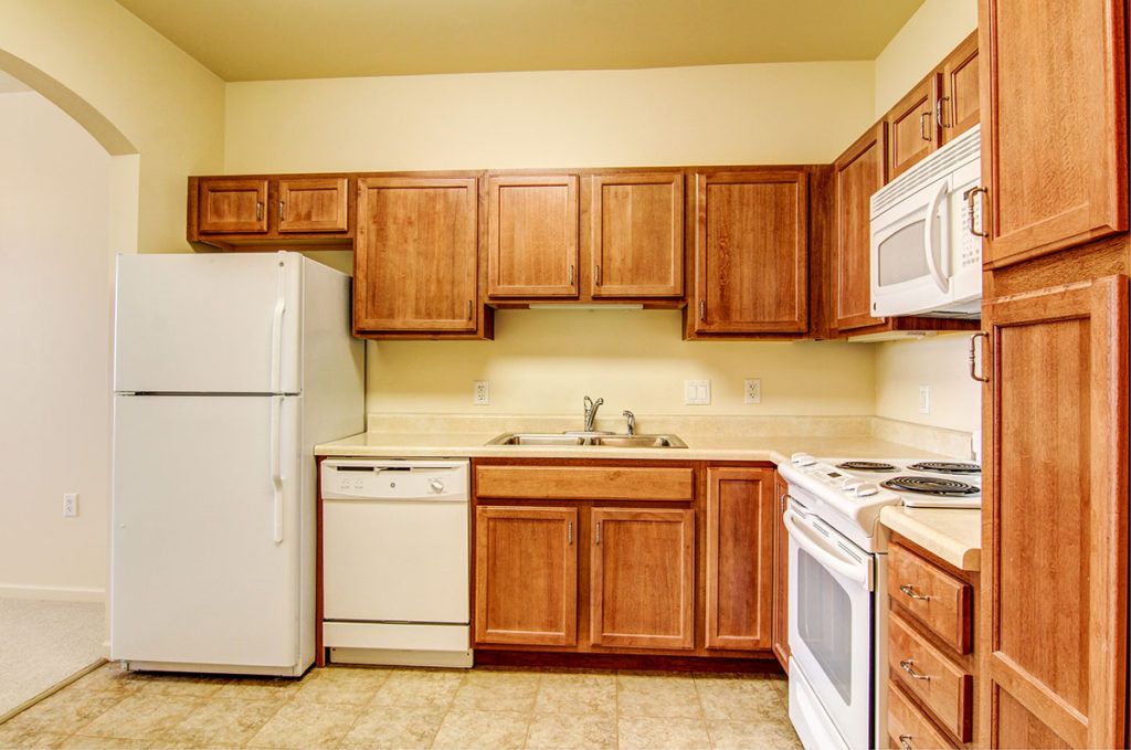 A kitchen with wooden cabinets and standard appliances including a refrigerator, dishwasher, microwave, and oven.