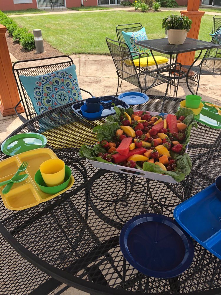 A vibrant outdoor dining setup features a table filled with an assortment of fruits and colorful plates on a patio.