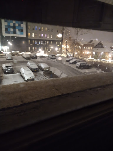 A view of a snowy parking lot at night, illuminated by city lights.